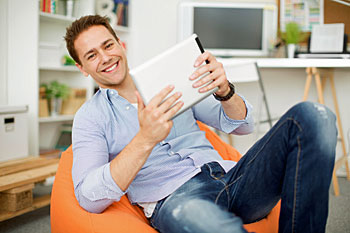 Mann sitzt mit Tablet in der Hand auf einem Sessel.