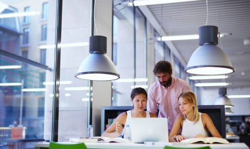 Zwei Frauen sitzen an Laptops und besprechen etwas mit einem männlichen Arbeitskollegen