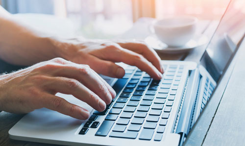 Zwei Hände einer Person tippen etwas auf einem Laptop