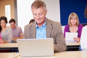 Ein älterer Mann sitzt mit einem Laptop in einer Vorlesung