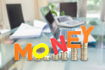 Münzstapel stehen nebeneinander auf einem Schreibtisch mit Laptop. Darüber steht das Wort 