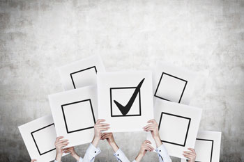 Viele Arme halten weiße Schilder hoch, auf dem ein schwarzes Viereck mit einem Haken zu sehen ist.