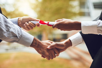 Ein Absolvent bekommt vom Dekan seine Abschlussurkunde mit Handschlag überreicht
