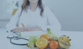Ernährungsberaterin sitzt an einem Tisch, auf dem Tisch liegen Dokumente, ein Stethoskop sowie Obst