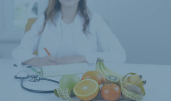 Eine Ärztin sitzt am Tisch vor verschiedenem Obst und einem Maßband.