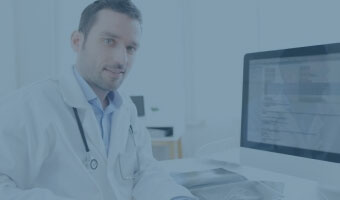 Ein Arzt sitzt am Schreibtisch vor seinem Rechner.