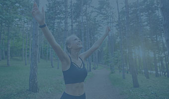 Eine Sportlerin steht mit hochgestreckten Armen im Wald.