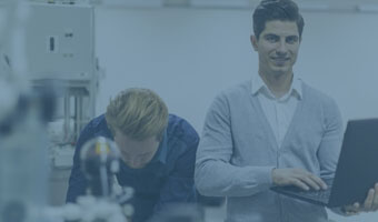 Zwei Ingeneure arbeiten in einer Werkstatt. Einer davon hält einen Laptop.