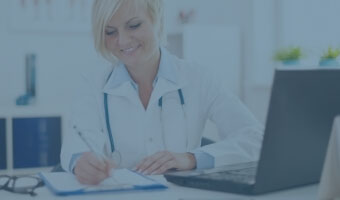 Eine Ärztin sitzt am Schreibtisch vor einem Laptop.