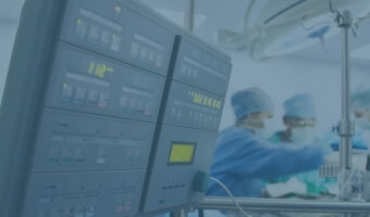 Zwei Chirurgen operieren im Hintergrund. Vorne ist eine medizinische Maschine zu sehen.