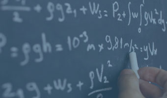 Jemand schreibt eine physikalische Formel mit Kreide an eine Tafel.