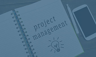 Ein Smartphone und ein Kugelschreiber liegen neben einem aufgeschlagenem Notizbuch in dem "project management" notiert ist.