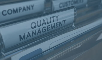 Ein Karteiordner mit dem Label "Quality Management" im Vordergrund.