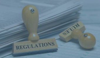 Vor einem Stapel Papier liegen zwei Stempel mit den Aufschriften "Regulations" und "Rules".