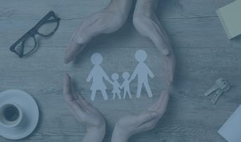 Auf einem Schreibtisch liegen eine Brille, ein Schlüssel, eine Espressotasse. Vier Hände formen einen Kreis um eine Familie, ausgeschnitten aus Papier.