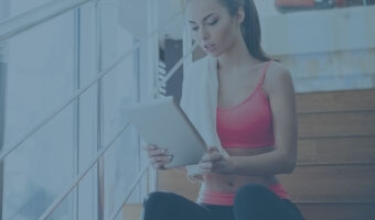 Eine junge Frau in Sportbekleidung sitzt auf einer Treppe und arbeitet an ihrem Tablet.