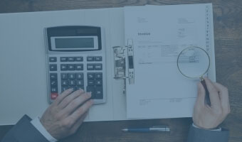 Ein Steuerberater arbeitet mit Taschenrechner und Lupe an einer aufgeschlagenen Akte.