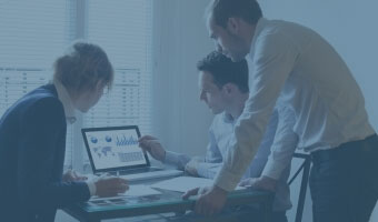 Drei Wirtschaftsinformatiker analysieren ein Diagramm an einem Rechner.