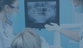 Drei Zahnmediziner betrachten das Röntgenbild eines menschlichen Kiefers.